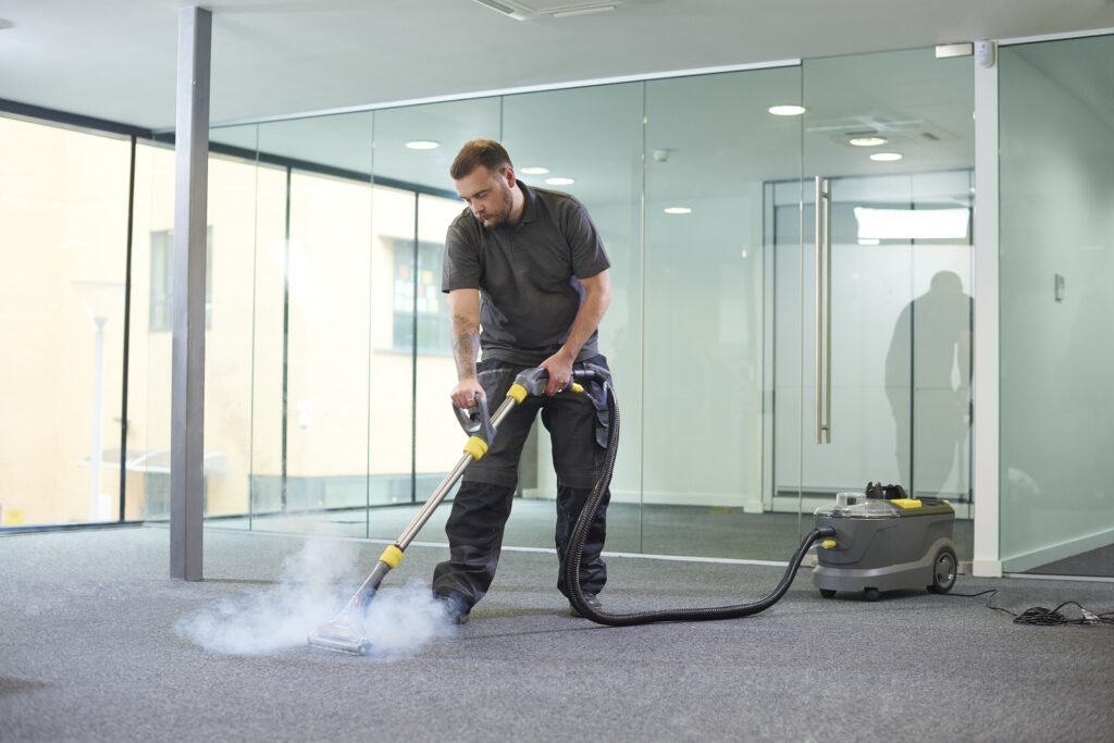 Worker steam cleaning carpet to remove dirt and grime.